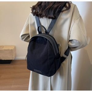 Detailed view of a black corduroy mini backpack worn over a beige trench coat