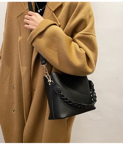 Détail du sac seau en cuir noir avec poignée tressée et boucles dorées sur modèle