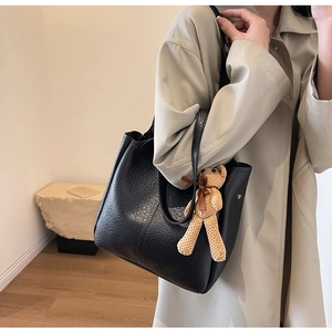 Detail of black pebbled leather tote bag with a cute brown bear charm and bow decoration