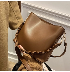 Détail du sac seau marron foncé avec bandoulière en cuir tressé et boucles dorées