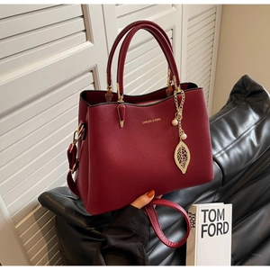 Macro detail of wine red litchi leather handbag with gold leaf pearl charm
