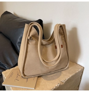 Close-up of beige canvas bucket bag with leather logo detail on a textured stone