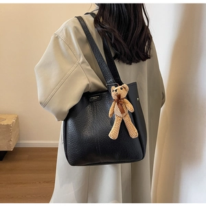 Detail of black textured tote bag with cute bear charm worn with a stylish khaki trench coat
