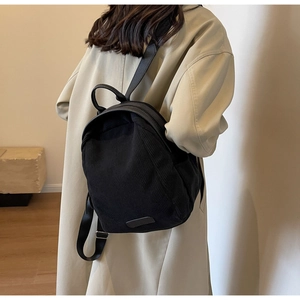 Close-up of the ribbed corduroy texture and dual zipper detail on the black backpack