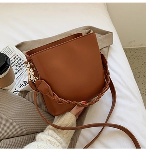 Détail d'un sac seau en cuir marron avec poignée tressée et boucles dorées chic