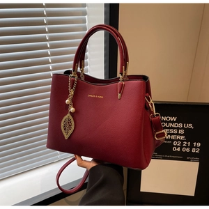Detail view of burgundy pebble leather handbag with gold leaf pendant and strap