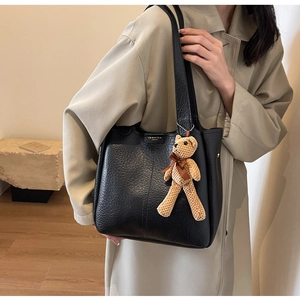Close-up of black lychee leather tote bag with gold logo and brown knit bear pendant
