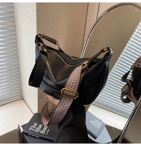 Détail d'un sac hobo en similicuir noir avec boucles dorées et large bandoulière à motifs