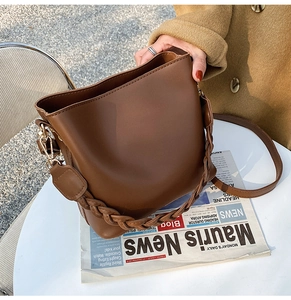 Vue détaillée du sac seau marron avec poignée tressée et crochets dorés latéraux