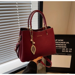 Close-up of wine red leather handbag featuring gold leaf pendant and pearl detail