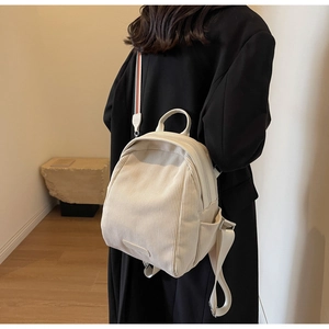 Detail view of cream corduroy mini backpack featuring colorful striped handle and soft texture