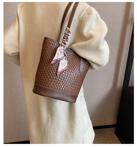 Detailed view of woven leather bucket bag with silk scarf on a model wearing a beige coat