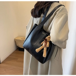 Black lychee leather tote bag with teddy bear charm shown on a beige trench coat