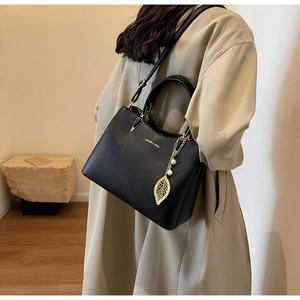 Detail showing litchi grain black leather texture and gold brand logo on tote bag