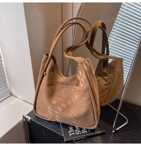 Detail of brown suede tote bag with front pocket and leather logo under natural light