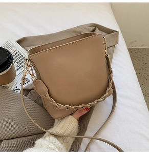 Détail du sac seau beige avec poignée tissée et boucles en métal doré sur fond textile