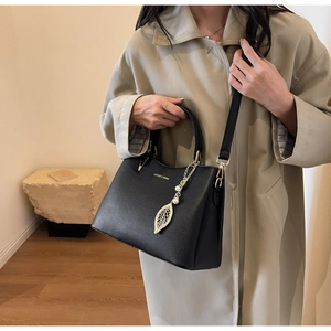 Chic black litchi texture handbag with gold leaf pendant styled on a trench coat
