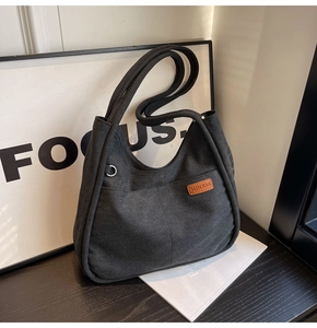 Detail of black canvas bucket bag featuring a brown leather label and wide shoulder straps