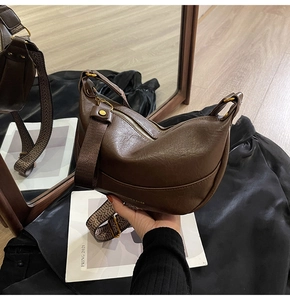 Détail du sac croissant en cuir marron foncé avec bandoulière tissée et grain texturé