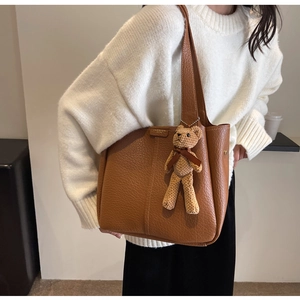Detail of brown litchi pattern leather tote bag with a cute beige crochet bear charm