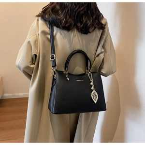 Structured black leather handbag with gold leaf pendant shown on a model in a long coat