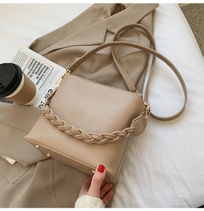 Détail du sac seau en cuir beige avec poignée tressée et pieds de protection dorés