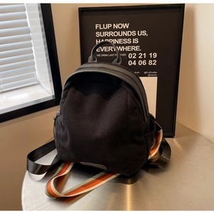 Close-up of black corduroy backpack featuring colorful striped straps and metal zippers