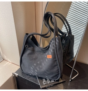 Detail of a black canvas tote bag with an orange leather patch and metal D-ring accent