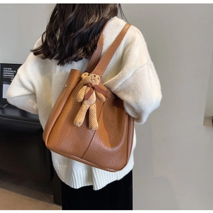Close-up of brown litchi pattern tote bag with a cute knitted bear charm on a model