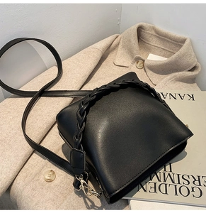 Détail du sac seau noir avec poignée tressée et boucles dorées sur fond élégant