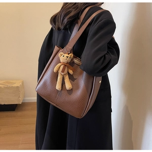 Detail of a brown faux leather tote bag with a beige knitted bear charm and thin straps