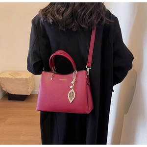 Detail of burgundy textured leather handbag with gold leaf charm and pearl accessories