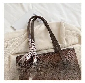 Detail of a brown woven leather tote bag featuring a geometric silk scarf on the handle