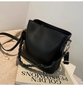 Détail du sac seau en cuir noir avec poignée tissée et finitions dorées sur livre