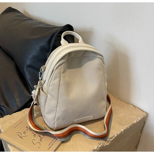 Detail of beige corduroy backpack with colorful striped strap on stone base
