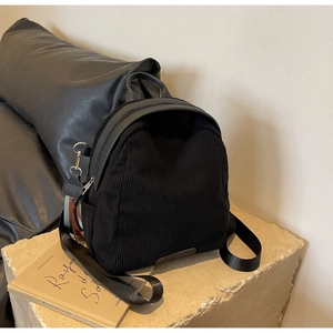 Detail of black corduroy backpack with leather handle on minimalist stone base