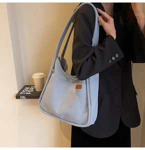 Detail of light blue minimalist canvas hobo bag with leather logo on casual suit