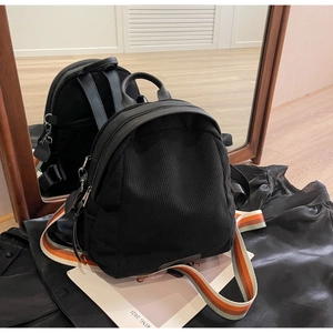 Detail of black corduroy backpack showing top leather handle and striped webbing straps