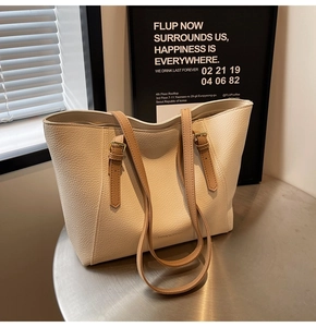 Détail d'un sac cabas en cuir crème texturé avec des bretelles réglables marron sur table