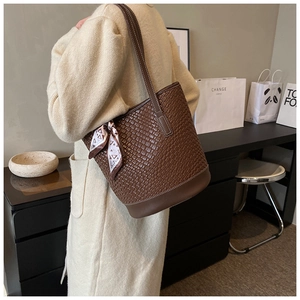 Brown woven leather bucket bag with silk scarf detail worn by model in minimalist room