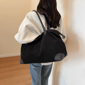Large capacity black corduroy tote bag with leather trim worn by a model in a room