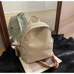 Detail of cream corduroy backpack with vibrant rainbow woven strap and metal zipper