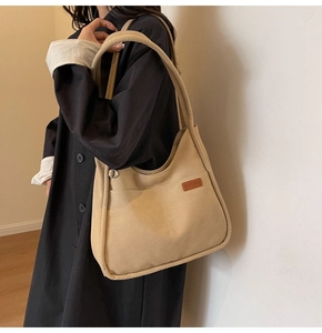Detail of beige canvas shoulder bucket bag with brown leather logo patch on a model