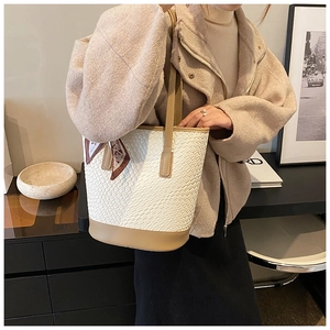 Detail of white woven tote bag featuring light brown leather base and geometric silk scarf