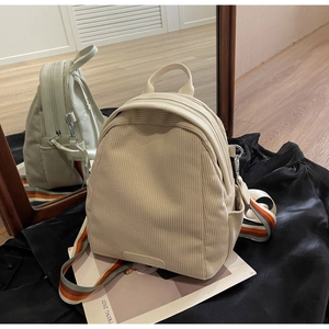 Detail view of cream corduroy backpack with multi-color striped strap and dual zippers