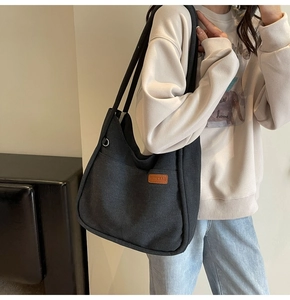 Detail of grey large canvas bucket bag with brown leather brand tag and metal ring buckle
