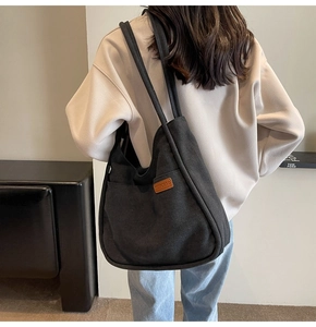 Detailed view of black canvas tote bag with brown leather logo patch and side pocket