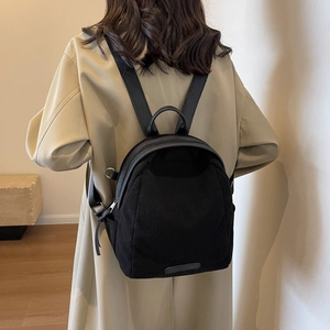Mini black corduroy backpack with leather straps worn by model in a stylish trench coat