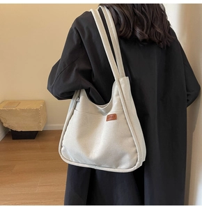 Detail of minimalist cream canvas bucket bag with leather brand logo and front pocket