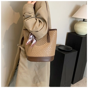 Detail of a large brown woven bucket bag with smooth leather trim and decorative silk scarf